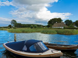 zwei kleine Boote liegen auf blauem Wasser, im Hintergrund ein Reetdachhaus